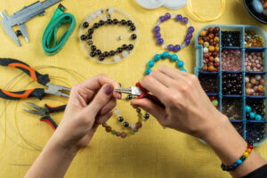 Fabrication de bijoux. Mains féminines avec un outil sur fond jaune.